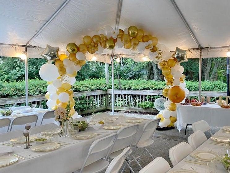 Gold and white balloon arch inside a tent, over set tables