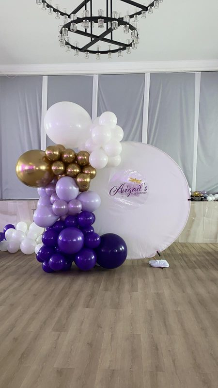 Purple, white and gold balloon garland beside a round backdrop