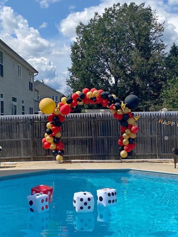 Red, black and gold balloon arch by a pool, with floating dice