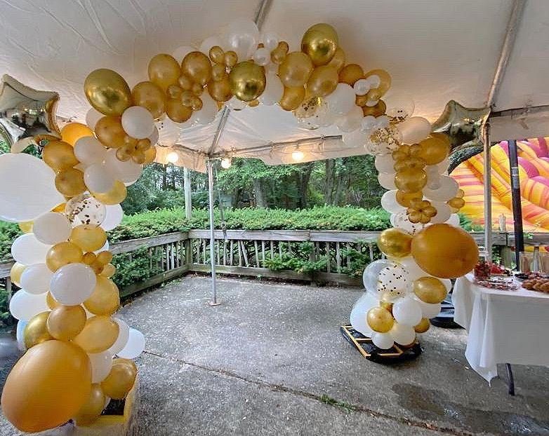 Gold and white balloon arch at the entrance of a tent